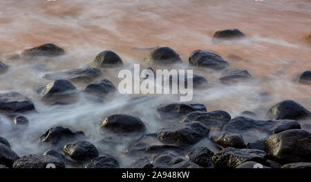 Wasserwaschung über Felsen am Strand bei Sonnenaufgang; Kauai, Hawaii, Vereinigte Staaten von Amerika Stockfoto