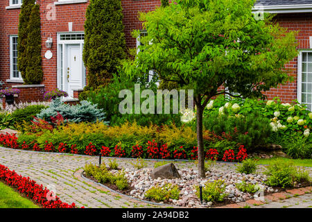 Herrliches Backsteinhaus mit einem gewundenen Pfad und Landschaftsgestaltung mit Pflanzen und Blumen im Vorgarten; Hudson, Quebec, Kanada Stockfoto