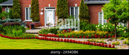 Herrliches Backsteinhaus mit einem gewundenen Pfad und Landschaftsgestaltung mit Pflanzen und Blumen im Vorgarten; Hudson, Quebec, Kanada Stockfoto