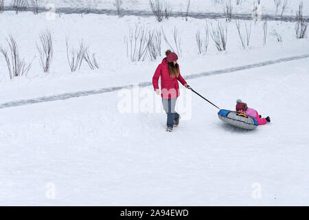 Aktive junge Mutter ihr Baby rollt auf einem Snow Tubing. Aktivitäten im Winter. Glück, ein Elternteil sein. Familie suchen. Stockfoto