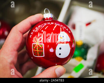 Red christmas Ball in einer Hand. Mit einer Aufschrift und einem Schneemann. Cute neue Jahre Geschenk. Mann Hand hält Red christmas Ball. Stockfoto