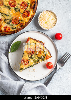 Zucchini Kuchen und Zutaten auf grauem Hintergrund, kopieren Raum rechts. Stück leckere herzhafte Kuchen mit Zucchini, Tomaten, Kräuter und Käse. Idee und Rezept für viel zu Ernten von Zucchini. Ansicht von oben Stockfoto