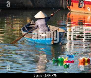 Frau paddeln eine hölzerne eye Boot in Hoi An, Vietnam mit bunten Papier Boote vom Full Moon Festival im Vordergrund. Stockfoto