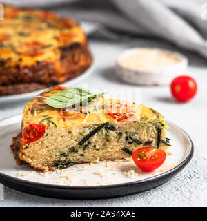 Zucchini Kuchen und Zutaten auf grauem Hintergrund, kopieren. Stück leckere herzhafte Kuchen mit Zucchini, Tomaten, Kräuter und Käse. Idee und Rezept für gesundes Backen und viel zu Ernten von Zucchini Stockfoto