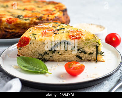 Zucchini Kuchen und Zutaten auf grauem Hintergrund, kopieren. Stück leckere herzhafte Kuchen mit Zucchini, Tomaten, Kräuter und Käse. Idee und Rezept für gesundes Backen und viel zu Ernten von Zucchini Stockfoto