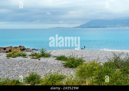 2019: Ein männlicher Erwachsener Einwanderer Spaziergänge entlang des Strandes von der italienischen Stadt Ventimiglia am Mittelmeer Riviera. Stockfoto