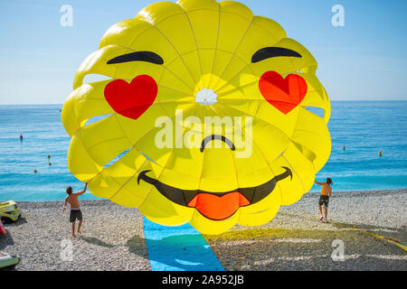 Zwei junge Männer führen ein glückliches Gesicht parasail Fallschirm, wie es der Strand an der Bucht der Engel Blätter an der Riviera in Nizza, Frankreich. Stockfoto