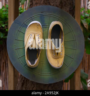 Schäbig ruiniert gelb Schuhe mit befestigt grün Dartscheibe Spiel Brett auf Baum im Garten zu grunge Stockfoto