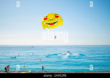 Touristen in Badekleidung zusehen, wie ein Boot mit Parasailing Paar über der Bucht der Engel nimmt an einem sonnigen Sommertag an der französischen Riviera Stockfoto