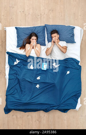 Bedtime. Junges Paar unter der Decke liegend auf Bett Draufsicht blasen Nase in das Gewebe unglücklichen Kranken Stockfoto