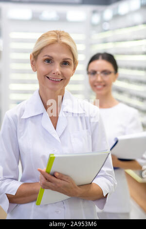 Erfahrenen Augenarzt. Blonde erfahrenen Augenarzt tragen weiße Fell holding Dokumente Stockfoto