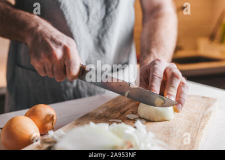 Unhöflich männliche Hände eine weiße Zwiebel mit einem Messer auf dem Hintergrund der Küche Stockfoto