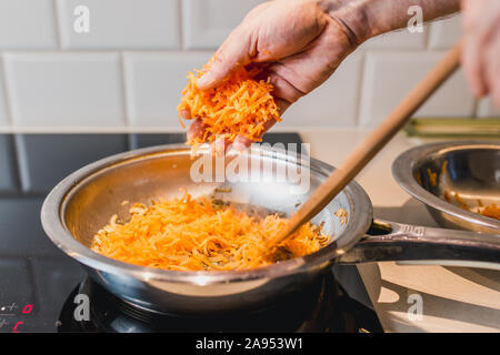 Kochen Pasta in einer Pfanne mit Sahnesauce - rauhe männliche Hände Karotten Stockfoto