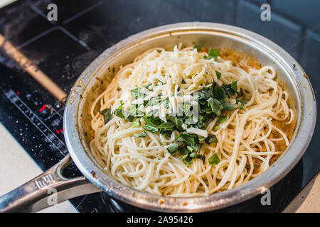 Spaghetti Pasta in einer cremigen Sauce in einer Pfanne mit gehacktem Basilikum, Käse und Gewürze - Kochen zu Hause Stockfoto