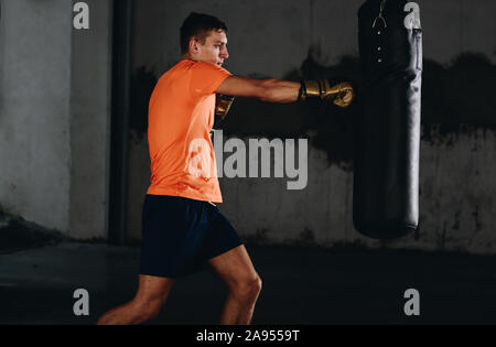 Junge Muskel Boxer mit einem Boxsack in der Turnhalle. Boxer schlagen Stanzgeschwindigkeit Tasche Stockfoto