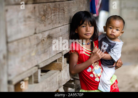 Ein junges Mädchen im Dorf Buscalan, Kalinga, Northern Luzon, Philippinen Holding ein Kind während gegen ein Gebäude schiefen Stockfoto