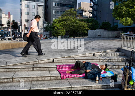 Männer Spaziergang vorbei an einem Obdachlosen schlafen auf dem Gehsteig Harumi Dori, Tokio, Japan. Stockfoto