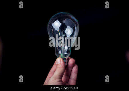 Die Glühbirne in der Hand vor schwarzem Hintergrund. Energie oder Idee, Konzept Stockfoto