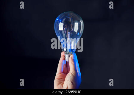 Die Glühbirne in der Hand vor schwarzem Hintergrund. Energie oder Idee, Konzept Stockfoto