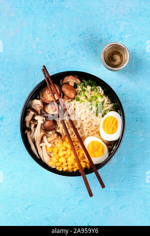 Ramen. Soba Nudeln mit gekochten Eiern, Shiitake-pilze, und Gemüse, Overhead shot auf einem blauen Hintergrund mit Stäbchen, eine Tasse Sake Stockfoto