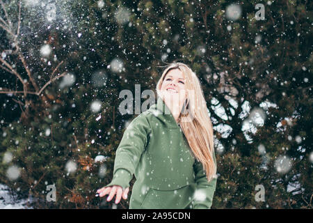 Schöne junge Frau wirft Schneeball - Outdoor Portrait im Winter bei Schneefall - attraktive Blondine Spaß hat Stockfoto