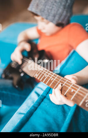 Nahaufnahme von einem Kind, das auf einem schwarzen E-Gitarre - Hand greift die Hinweise auf den Saiten-selektiven Fokus Stockfoto