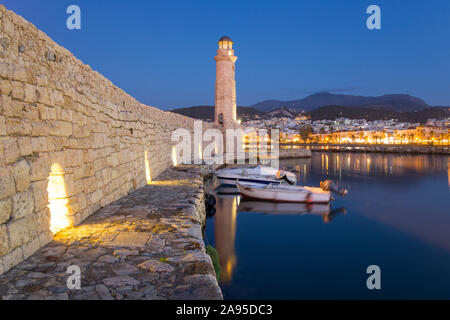 Rethymno, Kreta, Griechenland. Blick entlang der Mauer des venezianischen Hafens zum beleuchteten türkischen Leuchtturm aus dem 16. Jahrhundert, Abenddämmerung. Stockfoto