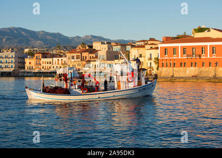 Chania, Kreta, Griechenland. Blick über den venezianischen Hafen bei Sonnenaufgang, Fischerboot auf dem Weg zum Meer. Stockfoto