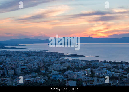 Chania, Kreta, Griechenland. Blick über die Stadt und den Golf von Chania bei Sonnenuntergang, die Insel Agii Theodori prominent. Stockfoto