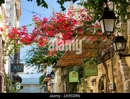 Rethymno, Kreta, Griechenland. Blick entlang Odos Xanthoudidou, Restaurantschilder und Bougainvillea prominent. Stockfoto