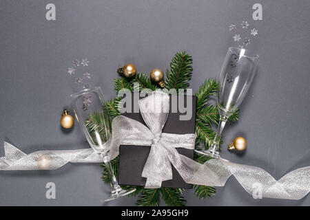 Weihnachtsfeiertag Komposition. Schwarz handgefertigte Geschenkboxen mit silber Farbband, Äste dekoriert, zwei Gläser Champagner Konfetti auf Grau backgroun Stockfoto