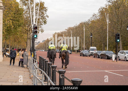 Rückansicht von zwei berittenen Polizisten, die gemeinsam auf Pferden die Mall, London, Großbritannien, hinauf reiten, nachdem sie gerade am Buckingham Palace vorbeigefahren sind. Stockfoto