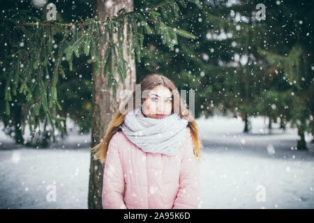 Junge attraktive braunhaarige Frau in eine warme Daunenjacke in einem verschneiten Wald im Winter unter den Tannen allein - verloren und kann den Weg nicht finden Stockfoto