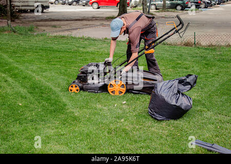 Ein Haushalt Garten Rasen Mähen mit schwarzer Tasche von Grasschnitt. Arbeiter sammelt gemähtem Gras in schwarzen Plastiktüten auf einer vor kurzem getrimmten Rasen Stockfoto