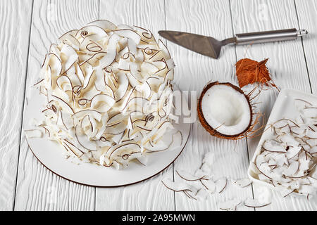 Nahaufnahme einer Kokos Kuchen mit Kokosnuss Bänder mit Zutaten auf einem weißen Tisch dekoriert Stockfoto
