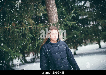 Junge attraktive braunhaarige Frau in eine warme Daunenjacke in einem verschneiten Wald im Winter unter den Tannen allein - verloren und kann den Weg nicht finden Stockfoto