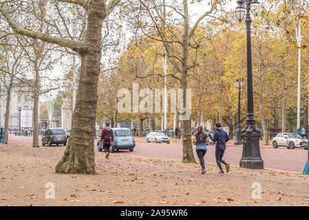 Männliches und weibliches Paar, Rückansicht, im Herbst auf dem Bürgersteig der Mall im Zentrum von London in Großbritannien, joggen in Richtung Buckingham Palace. Stockfoto