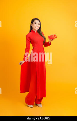 Lächelnd asiatische Frau mit Geschenkbox und tragen Ao Dai Vietnam. Über gelb Hintergrund isoliert Stockfoto