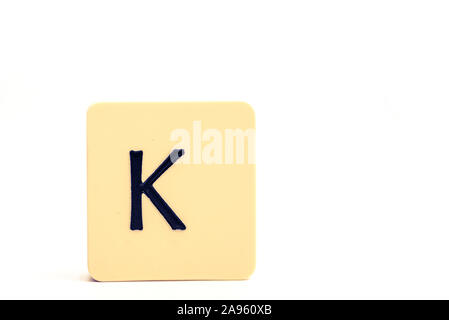 Dunkle Buchstabe K auf ein helles gelbes Quadrat auf weißem Hintergrund Stockfoto