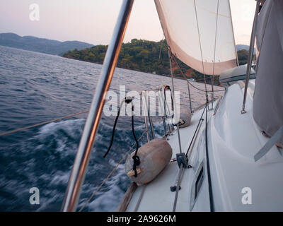 Rückenwind, das Konzept der sich vorwärts zu bewegen, auf alle Segel. Bootsfahrt auf einer Yacht unter Segeln, ein Fragment des Decks und die Berge am Horizont. Stockfoto