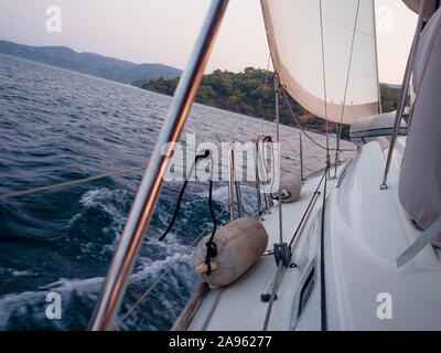 Rückenwind, das Konzept der sich vorwärts zu bewegen, auf alle Segel. Bootsfahrt auf einer Yacht unter Segeln, ein Fragment des Decks und die Berge am Horizont. Stockfoto