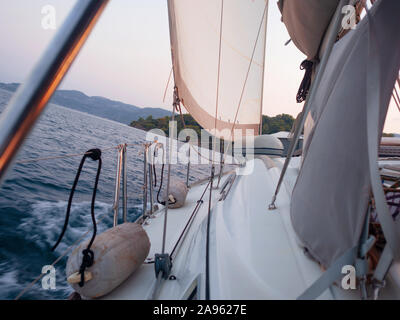 Rückenwind, das Konzept der sich vorwärts zu bewegen, auf alle Segel. Bootsfahrt auf einer Yacht unter Segeln, ein Fragment des Decks und die Berge am Horizont. Stockfoto