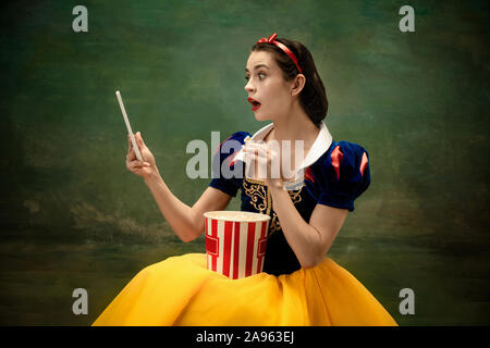 Junge Ballett Tänzerin als Schneewittchen mit Tablet suchen Kino mit Popcorn. Flexible Ballerina als Zeichen von fairytail in helle Kleidung. Moderne Geschichte im klassischen Märchen. Emotionen, Vergleich der Epochen. Stockfoto