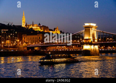 Die Chain Bridge bei Nacht beleuchtet mit Schloss Buda und die Turmspitze der Matthias Kirche im Hintergrund Stockfoto