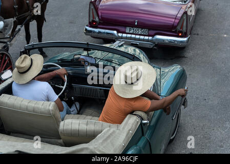 Ein Fahrer und seine Kollegin, die traditionelle Kubanische Hut mit breiter Krempe aus Palmblättern, in ihren amerikanischen Cabrio Oldtimer, versuchen zu Attr Stockfoto