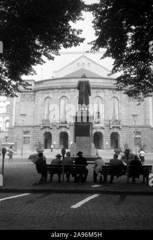 Mainzer in Artikel Bänken auf dem Gutenbergplatz und blicken in das Gutenbergdenkmal und das Stadttheater in Mainz, Deutschland 1961. Bewohner von Mainz sitzen auf Bänken am Gutenbergplatz Square, mit Blick auf die Rückseite des Gutenberg Monument und dem Stadttheater, Deutschland 1961. Stockfoto