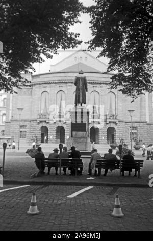 Mainzer in Artikel Bänken auf dem Gutenbergplatz und blicken in das Gutenbergdenkmal und das Stadttheater in Mainz, Deutschland 1961. Bewohner von Mainz sitzen auf Bänken am Gutenbergplatz Square, mit Blick auf die Rückseite des Gutenberg Monument und dem Stadttheater, Deutschland 1961. Stockfoto