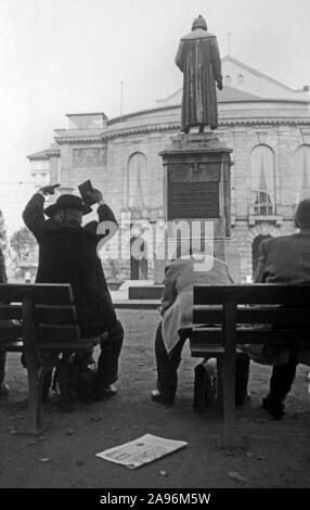 Mainzer in Artikel Bänken auf dem Gutenbergplatz und blicken in das Gutenbergdenkmal und das Stadttheater in Mainz, Deutschland 1961. Bewohner von Mainz sitzen auf Bänken am Gutenbergplatz Square, mit Blick auf die Rückseite des Gutenberg Monument und dem Stadttheater, Deutschland 1961. Stockfoto