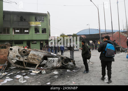 La Paz, Bolivien. 12 Nov, 2019. Menschen stehen neben einem Ausgebrannten Auto und eine zerstörte Polizeistation. Nach dem Rücktritt des bolivianischen Präsidenten Morales, marodierende Banden in dem südamerikanischen Land sind bis zu nicht gut - jetzt die Militärs wollen, dem Spuk ein Ende zu setzen. Credit: Gaston Brito/dpa/Alamy leben Nachrichten Stockfoto