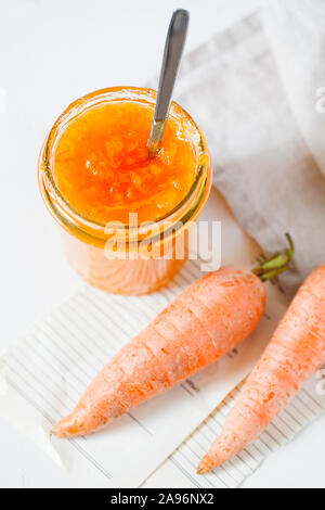 Vegetarische Karotte Konfitüre oder Marmelade mit Orangensaft in einem Glas auf einem weißen Hintergrund. gesundes organisches Gemüse Dessert zum Frühstück. Vertikale Ori Stockfoto